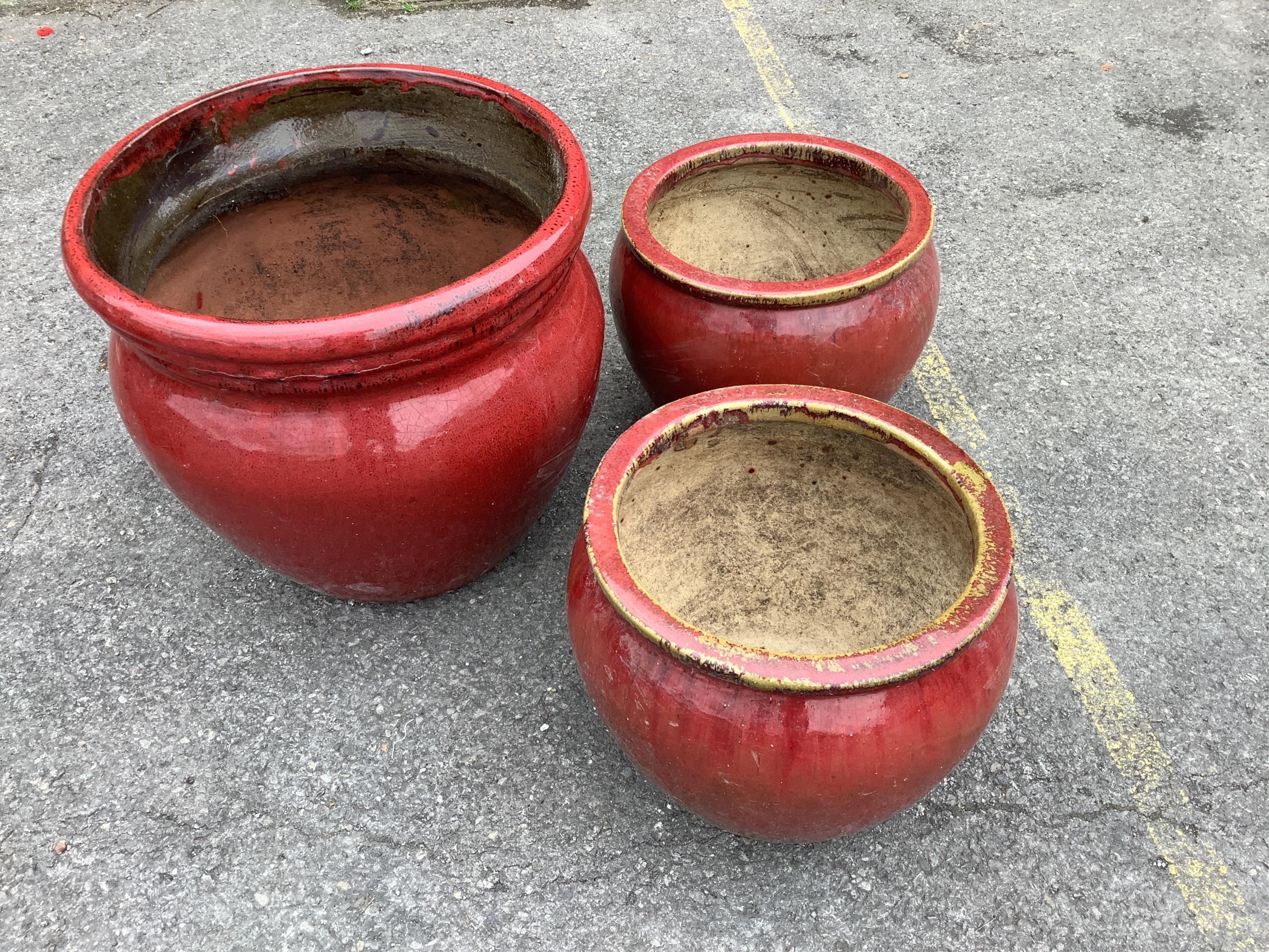A set of three graduated red glazed circular earthenware garden planters, largest diameter 49cm, height 45cm